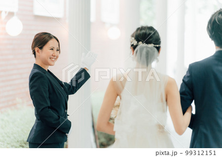 結婚式場を案内するウェディングプランナー・ドアスタッフ・ホテリエの女性と新郎新婦（結婚式） 99312151
