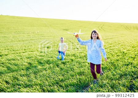 Cheerful and happy children play in the field and imagine themselves to be pilots on a sunny summer day. Kids dreams of flying and aviation. Cheerful and happy children play in the field and imagine themselves to be pilots on a sunny summer day. Kids dreams of flying and aviation. 99312425