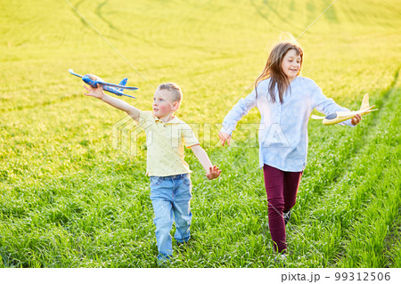 Cheerful and happy children play in the field and imagine themselves to be pilots on a sunny summer day. Kids dreams of flying and aviation. Cheerful and happy children play in the field and imagine themselves to be pilots on a sunny summer day. Kids dreams of flying and aviation. 99312506