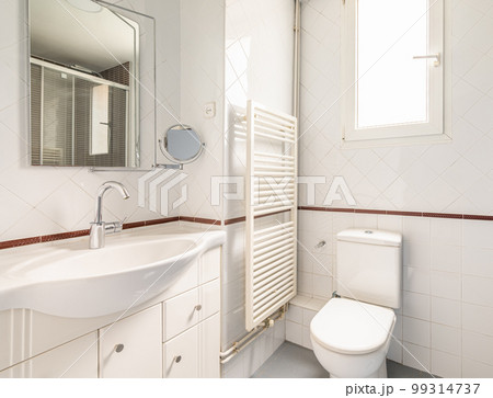 Cozy bright white bathroom with diamond shaped tiles with a window for natural light toilet sink and heated towel rail and mirror. Concept of modern cozy bathroom 99314737