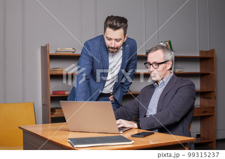 Mature businessman in blue suit and his younger colleague are working on the laptop 99315237