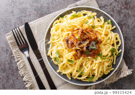 Kasespatzle delicious spatzle noodles with cheese and fried onion top close-up in a plate. Horizontal top view 99315424