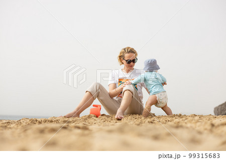 Mother playing his infant baby boy son on sandy beach enjoying summer vacationson on Lanzarote island, Spain. Family travel and vacations concept Mother playing his infant baby boy son on sandy beach enjoying summer vacationson on Lanzarote island, Spain. Family travel and vacations concept 99315683