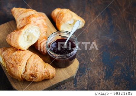 Freshly baked croissants with jam on dark wooden background. 99321305