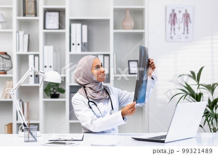 Young successful female doctor in hijab working in clinic inside medical office, muslim woman is angry and thinking x-ray picture sitting at workplace with laptop. Young successful female doctor in hijab working in clinic inside medical office, muslim woman is angry and thinking x-ray picture sitting at workplace with laptop. 99321489