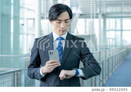 スマホを手にスマートウォッチを見る若いビジネスマン 99322005