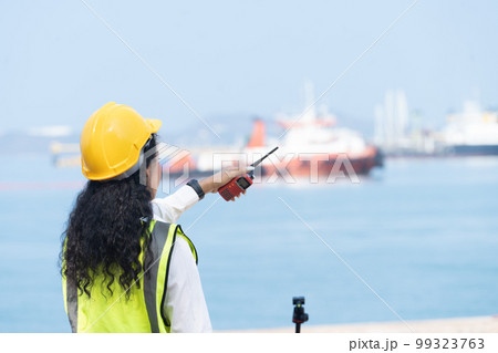 Asian Female Engineer Holding Walkie-Talkie with Marine Ship Background 99323763