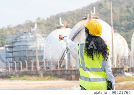 female engineer with hardhat with petrochemical factory background. asian woman holding tablet, plan and Walkie Talkie. 99323766