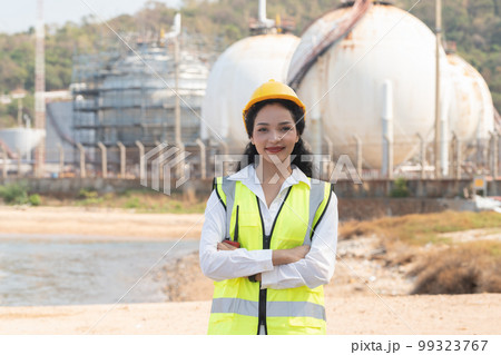 female engineer with hardhat with petrochemical factory background. asian woman holding tablet, plan and Walkie Talkie. 99323767