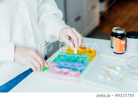 Woman's hands sorting pills into pills organizer. Weekly medical pill box with daily doses of medicines. Antioxidant diet vitamin supplements for health and beauty care, biohacking concept Woman's hands sorting pills into pills organizer. Weekly medical pill box with daily doses of medicines. Antioxidant diet vitamin supplements for health and beauty care, biohacking concept 99325795