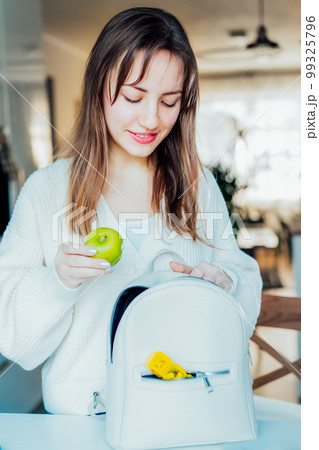 Woman putting apple and daily pills organizer into her bag. Taking daily medicine antioxidant diet vitamin supplements for beauty skin hair health care medicament biohacking concept. Selective focus. 99325796