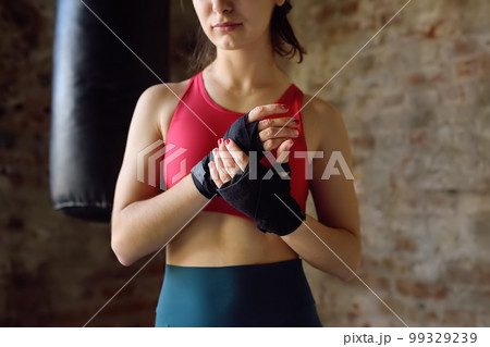 Young female boxer preparing for boxing fight. Athletic woman wearing strap on wrist before boxing practice in gym. Healthy lifestyle 99329239