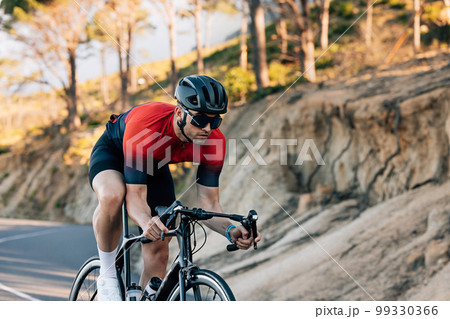 Professional cyclist going down a hill. Athlete in helmet and glasses riding road bike outdoors. Professional cyclist going down a hill. Athlete in helmet and glasses riding road bike outdoors. 99330366