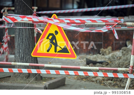 Warning roadworks sign and safety barrier on city street during maintenance repair work Warning roadworks sign and safety barrier on city street during maintenance repair work 99330858