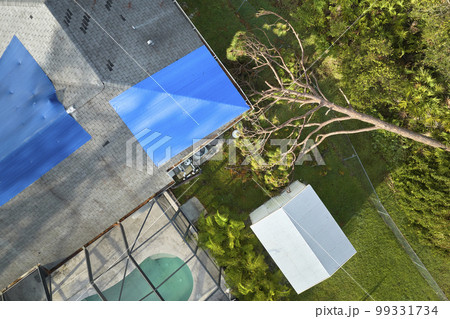 Hurricane Ian damaged house rooftop covered with protective plastic tarp against rain water leaking until replacement of asphalt shingles. Aftermath of natural disaster 99331734