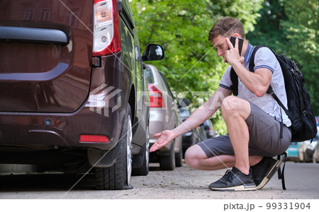 Driver calling road service for assistance having vehicle trouble with punctured flat tire on car parked on roadside Driver calling road service for assistance having vehicle trouble with punctured flat tire on car parked on roadside 99331904