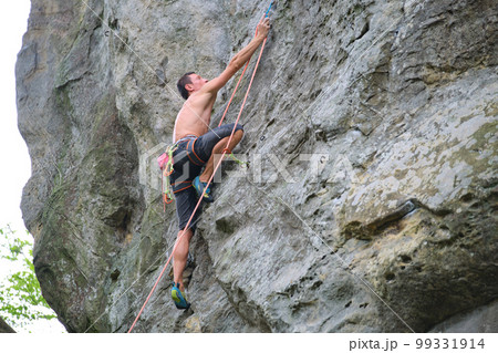 Determined climber clambering up steep wall of rocky mountain. Sportsman overcoming difficult route. Engaging in extreme sports and rock climbing hobby concept. Determined climber clambering up steep wall of rocky mountain. Sportsman overcoming difficult route. Engaging in extreme sports and rock climbing hobby concept. 99331914