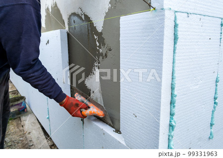 Construction worker installing styrofoam insulation sheets on house facade wall for thermal protection. 99331963