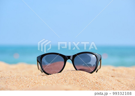 Closeup of black protective sunglasses on sandy beach at tropical seaside on warm sunny day. Summer vacation concept. Closeup of black protective sunglasses on sandy beach at tropical seaside on warm sunny day. Summer vacation concept. 99332108