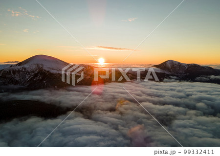 Aerial view of vibrant sunrise over white dense fog with distant dark Carpathian mountains on horizon. 99332411