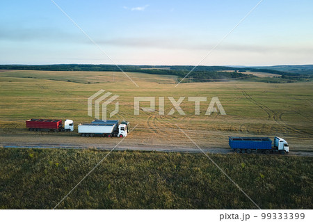 Aerial view of cargo truck driving on dirt road between agricultural wheat fields making lot of dust. Transportation of grain after being harvested by combine harvester during harvesting season Aerial view of cargo truck driving on dirt road between agricultural wheat fields making lot of dust. Transportation of grain after being harvested by combine harvester during harvesting season 99333399
