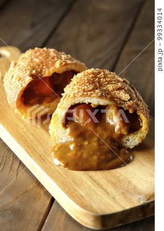 カッティングボードの上の半分にカットされルーが流れ出るカレーパン 99334014