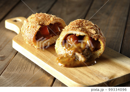 カッティングボードの上の半分にカットされルーが流れ出るゴロゴロ野菜と牛肉入りカレーパン 99334096