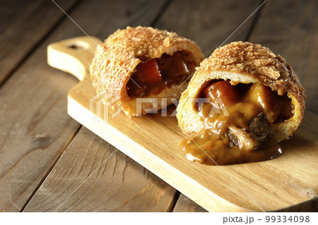 カッティングボードの上の半分にカットされルーが流れ出るゴロゴロ野菜と牛肉入りカレーパン カッティングボードの上の半分にカットされルーが流れ出るゴロゴロ野菜と牛肉入りカレーパン 99334098