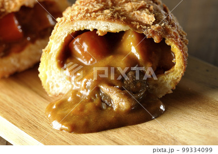 カッティングボードの上の半分にカットされルーが流れ出るゴロゴロ野菜と牛肉入りカレーパン カッティングボードの上の半分にカットされルーが流れ出るゴロゴロ野菜と牛肉入りカレーパン 99334099