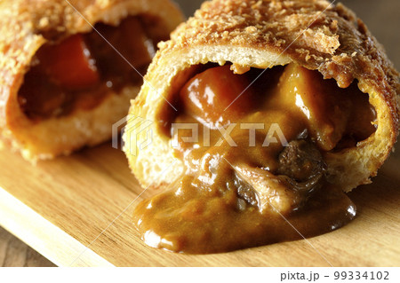 カッティングボードの上の半分にカットされルーが流れ出るゴロゴロ野菜と牛肉入りカレーパン カッティングボードの上の半分にカットされルーが流れ出るゴロゴロ野菜と牛肉入りカレーパン 99334102
