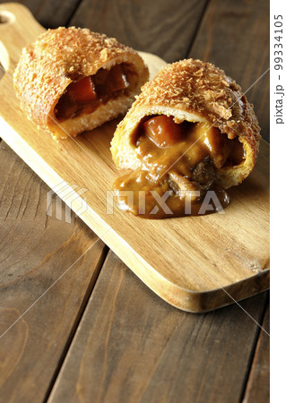 カッティングボードの上の半分にカットされルーが流れ出るゴロゴロ野菜と牛肉入りカレーパン 99334105