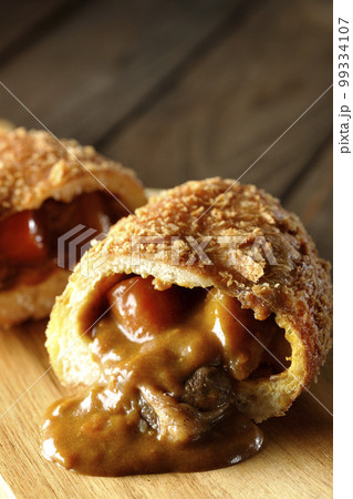 カッティングボードの上の半分にカットされルーが流れ出るゴロゴロ野菜と牛肉入りカレーパン カッティングボードの上の半分にカットされルーが流れ出るゴロゴロ野菜と牛肉入りカレーパン 99334107