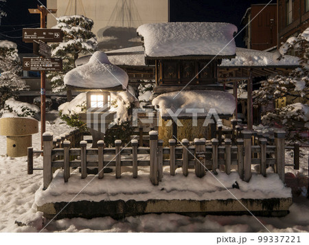 雪が積もった街中のお社 99337221