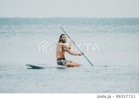 Sea woman and man on sup. Silhouette of happy young woman and man, surfing on SUP board, confident paddling through water surface. Idyllic sunset. Active lifestyle at sea or river. 99337731
