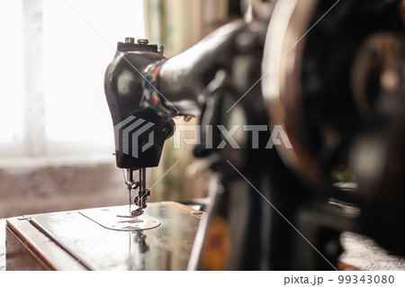 An old sewing machine stands on the table at home ready to work and sew. Classic retro style manual sewing machine ready for sewing work. The machine is old style made of metal with floral patterns An old sewing machine stands on the table at home ready to work and sew. Classic retro style manual sewing machine ready for sewing work. The machine is old style made of metal with floral patterns 99343080