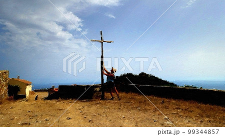 A woman prays at the foot of a wooden cross. 99344857