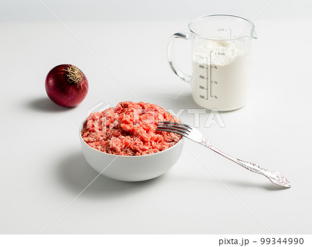 Plate with fresh ground beef and fork, red onion, measuring cup with flour on a white background, space for text, stock photo Plate with fresh ground beef and fork, red onion, measuring cup with flour on a white background, space for text, stock photo 99344990