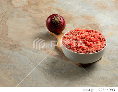 Plate with fresh ground beef, onion on a brown vintage background, space for text, stock photo Plate with fresh ground beef, onion on a brown vintage background, space for text, stock photo 99344993