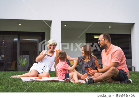 Family picnic on a sunny summer day, their house in the background Family picnic on a sunny summer day, their house in the background 99346756