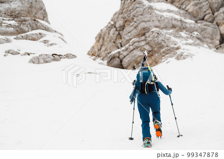 One lonely ski tourer climbing up the snowy mountain, view from behind 99347878