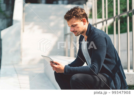 Caucasian man working on the tablet during his lunch break, sitting outside in the sun 99347908