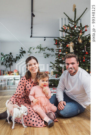 Vertical portrait of young caucasian family with baby girl and a chihuahua in front of the Christmas tree Vertical portrait of young caucasian family with baby girl and a chihuahua in front of the Christmas tree 99348125
