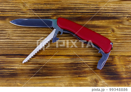 Red all purpose pocket knife on a rustic wooden background. Top view Red all purpose pocket knife on a rustic wooden background. Top view 99348886