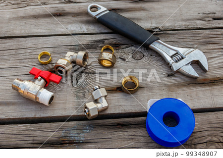 Various plumbing spare parts, sealing tape and adjustable wrench on rustic wooden background. Top view 99348907