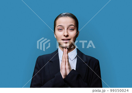 Young female pleading holding her palms together in request, on blue background 99350024