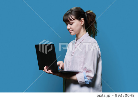 Serious female student looking at laptop screen, on blue background 99350048