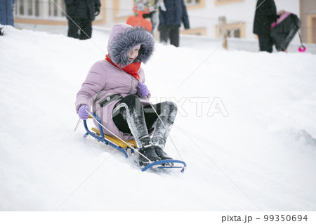 A girl warmly dressed sledding on a cold winter day. 99350694
