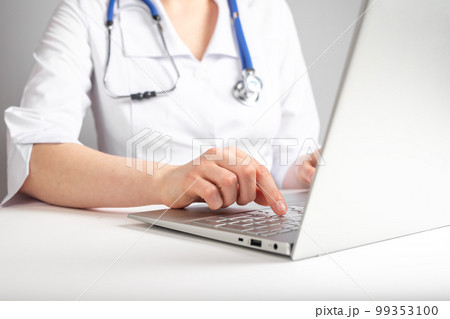 Doctor with stethoscope typing on laptop keyboard. Health care and medicine concept. Woman in lab coat sitting at desk with computer and prescribing medications. Doctor with stethoscope typing on laptop keyboard. Health care and medicine concept. Woman in lab coat sitting at desk with computer and prescribing medications. 99353100