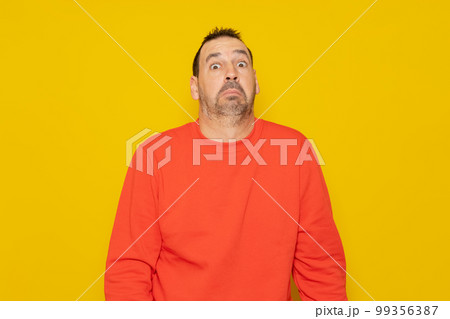 Bearded latino man wearing a red sweater with expression of doubt and confusion shrugging shoulders isolated over yellow background. Bearded latino man wearing a red sweater with expression of doubt and confusion shrugging shoulders isolated over yellow background. 99356387