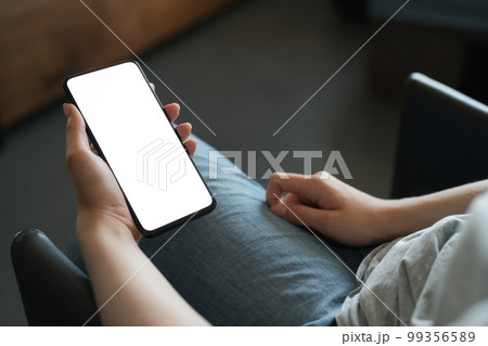 Young woman sitting in chair and holding smartphone with white screen Young woman sitting in chair and holding smartphone with white screen 99356589